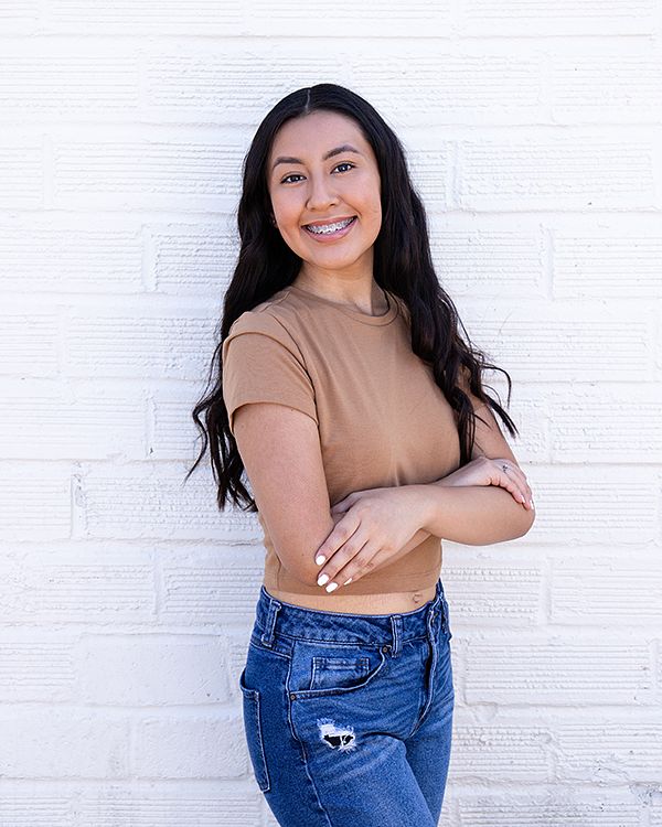 Senior with folded arms against a white brick wall