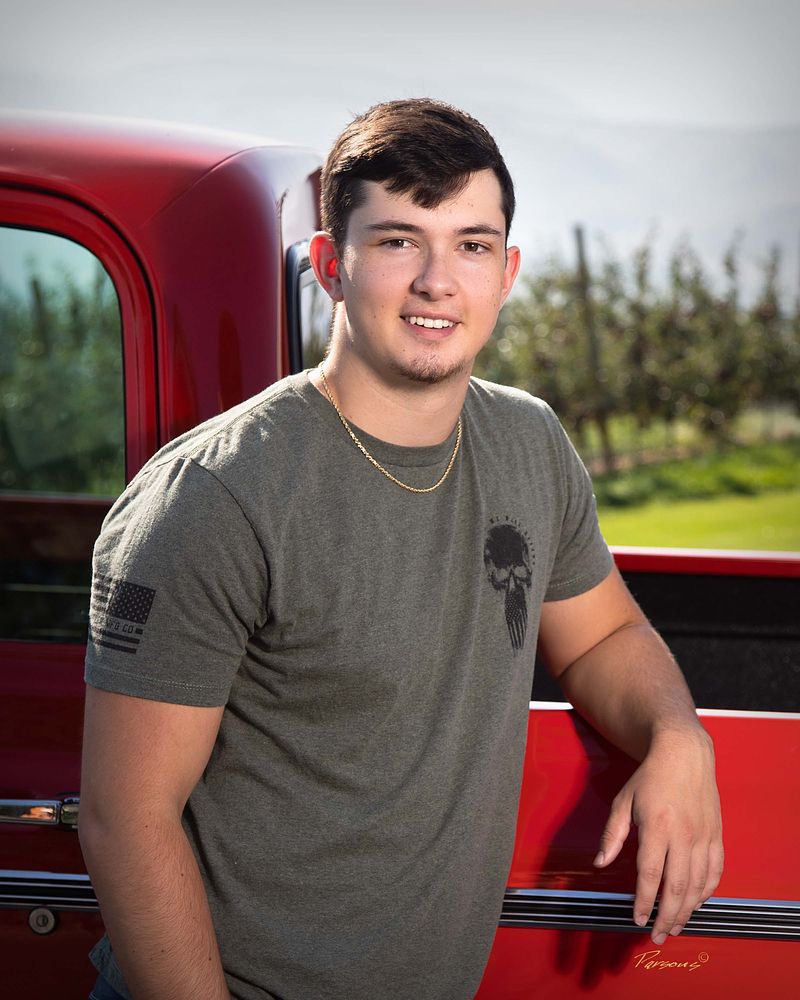 Senior leaning on a red pickup truck beside an orchard
