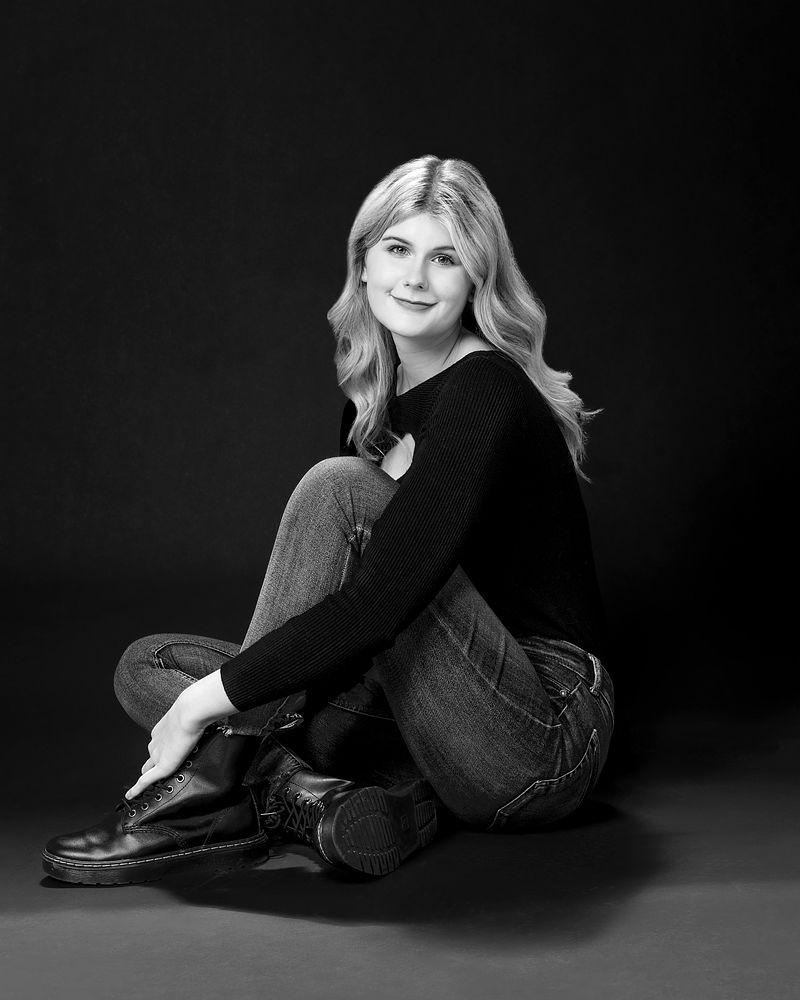 Black-and-white studio portrait of a senior sitting on the floor